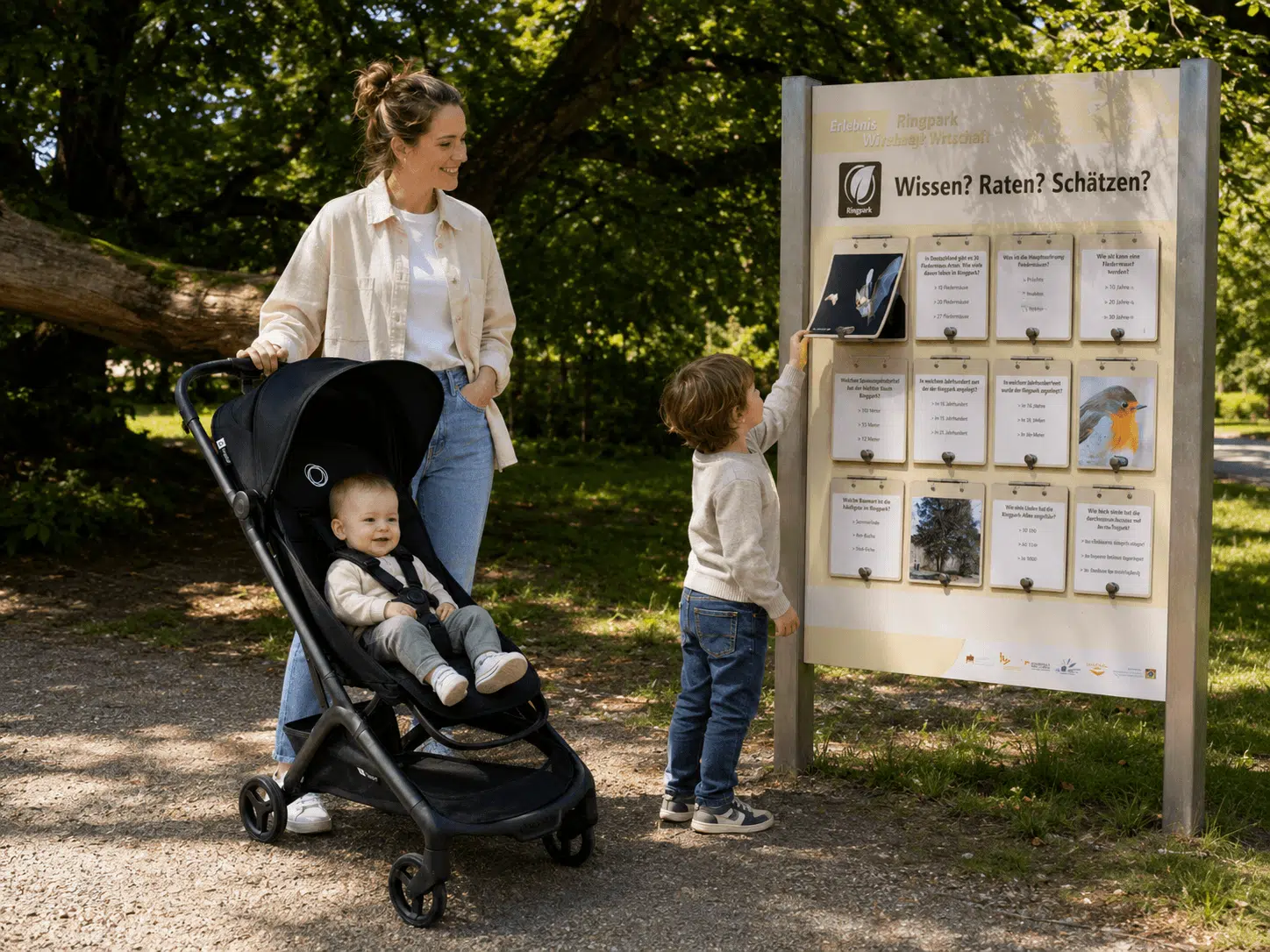 Mama mit Kinderwagen und zwei Kindern an der Quiz-Tafel im Ringpark Würzburg.